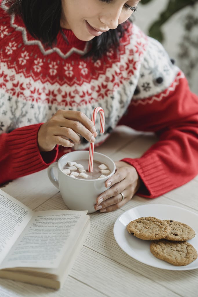 Person in Red Christmas Sweater Holding White Ceramic Cup With Hot Chocolate Drink