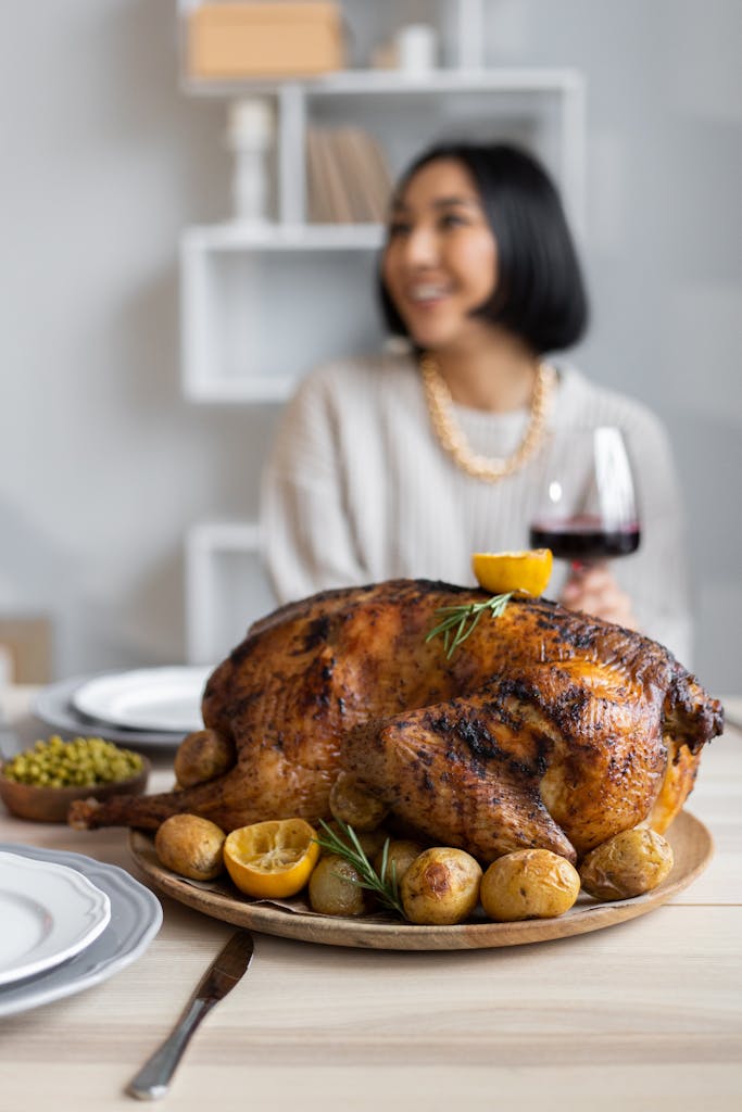 Blurred Asian woman with glass of wine sitting at table with appetizing roasted turkey cooked for celebrating Thanksgiving