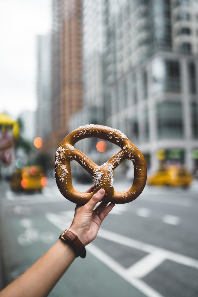 Close-up of a hand holding a salted pretzel against a bustling New York City street backdrop.