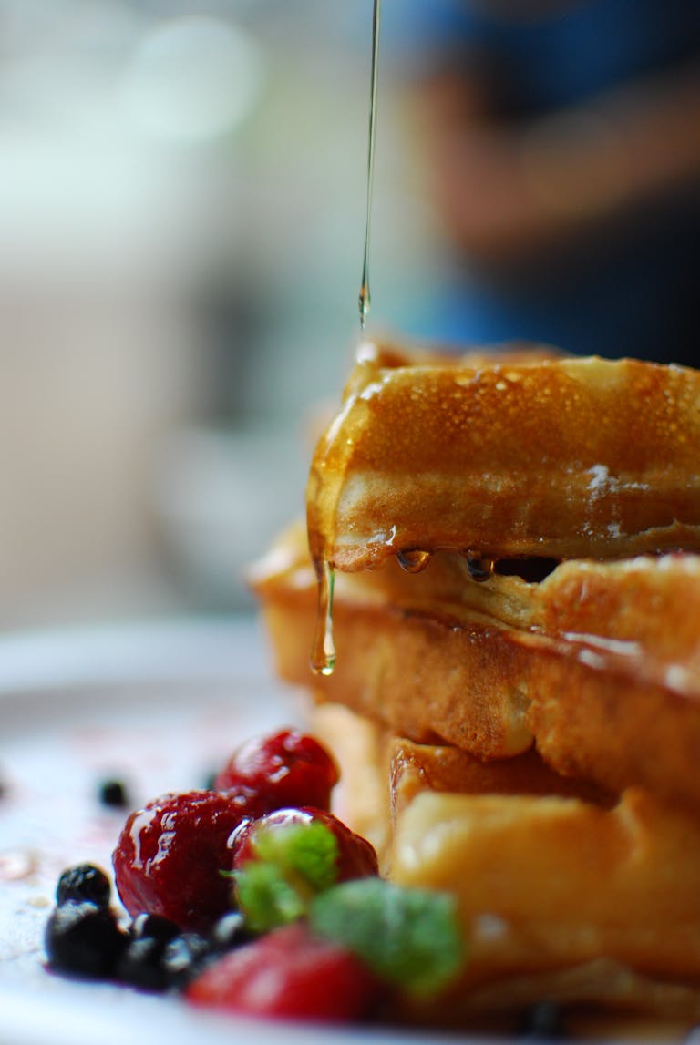 Syrup drips onto stacked waffles with fresh berries, a breakfast delight.