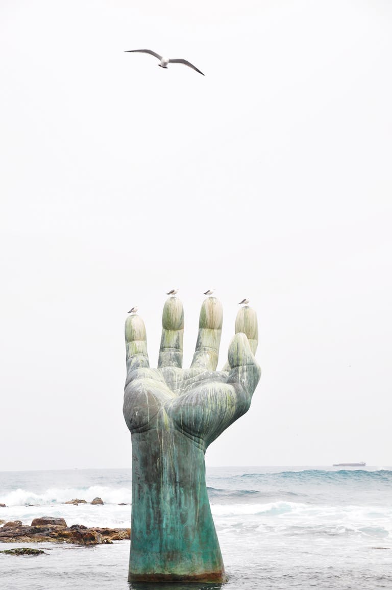 A striking sculpture rises from the sea, reaching toward the sky with seagulls resting on it.