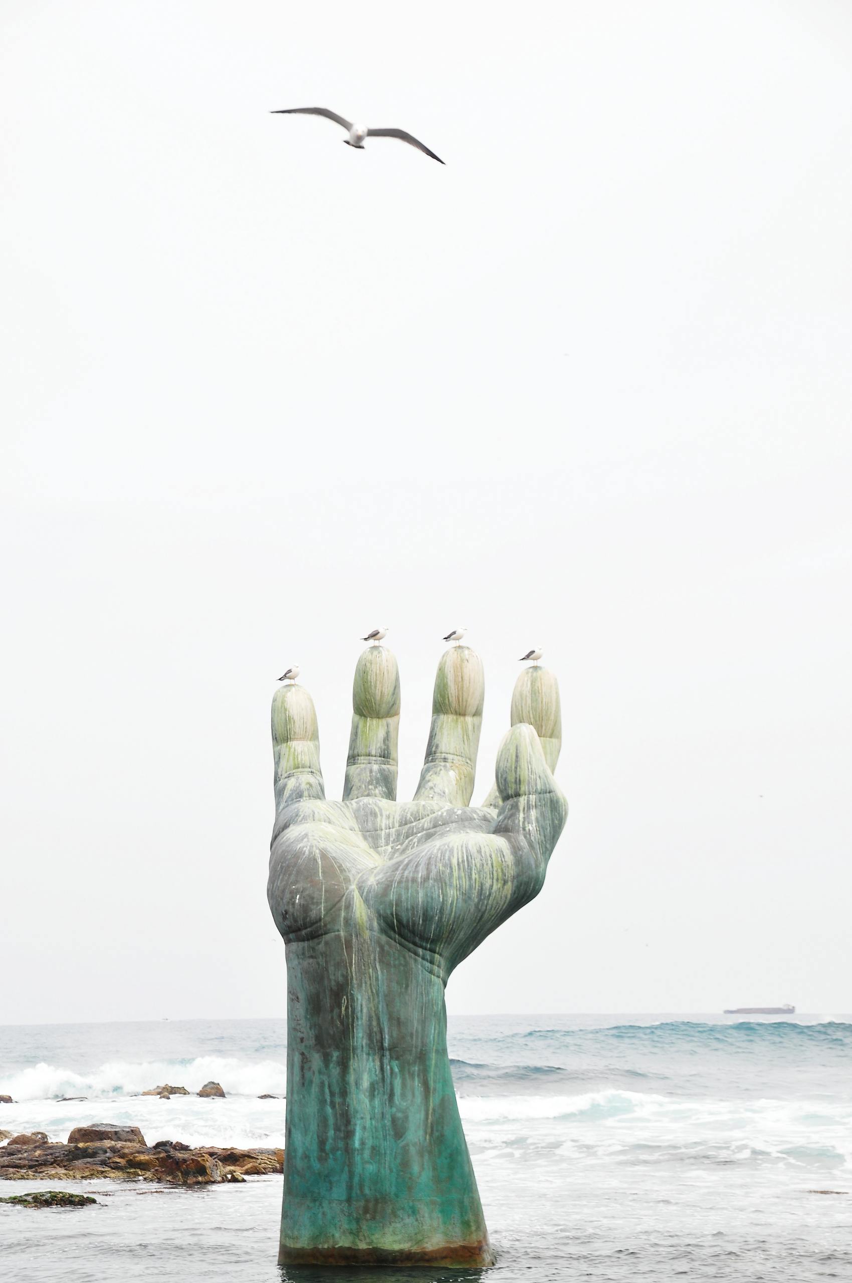 A striking sculpture rises from the sea, reaching toward the sky with seagulls resting on it.