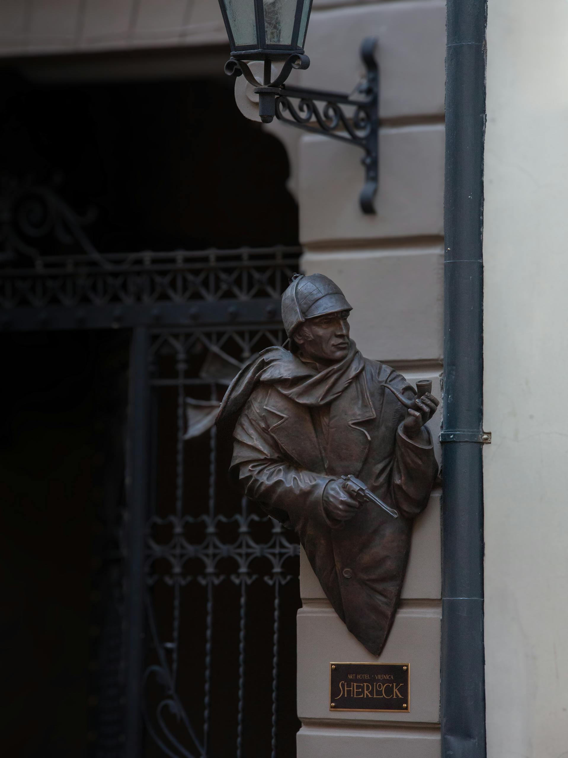 Bronze statue of Sherlock Holmes on a building facade in Riga, Latvia, depicting iconic character in urban setting.