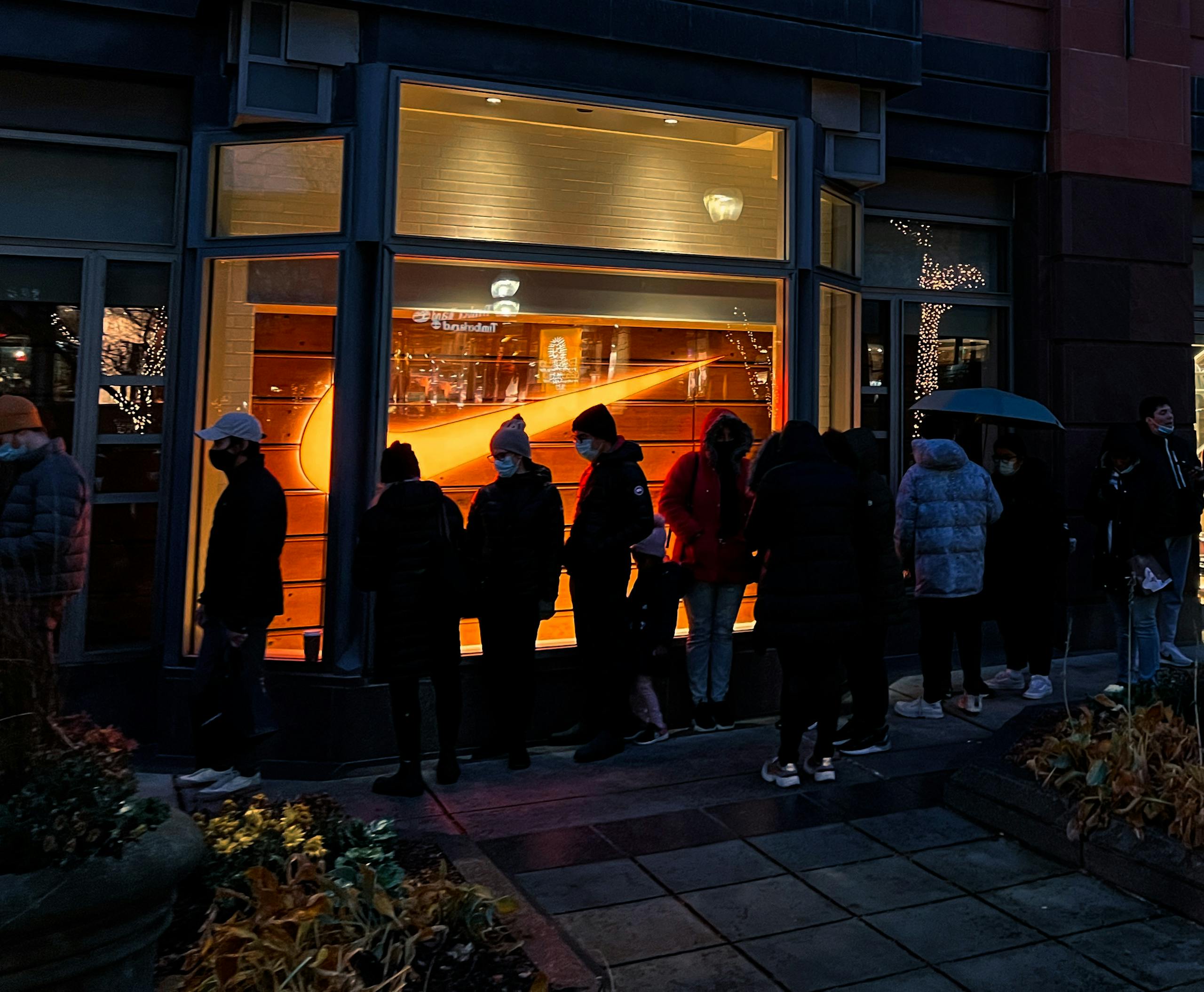 Individuals waiting in line outside a well-lit store at night, possibly during a sale event.