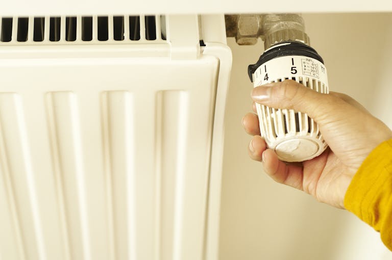 Close-up of hand adjusting radiator thermostat to control home heating temperature.