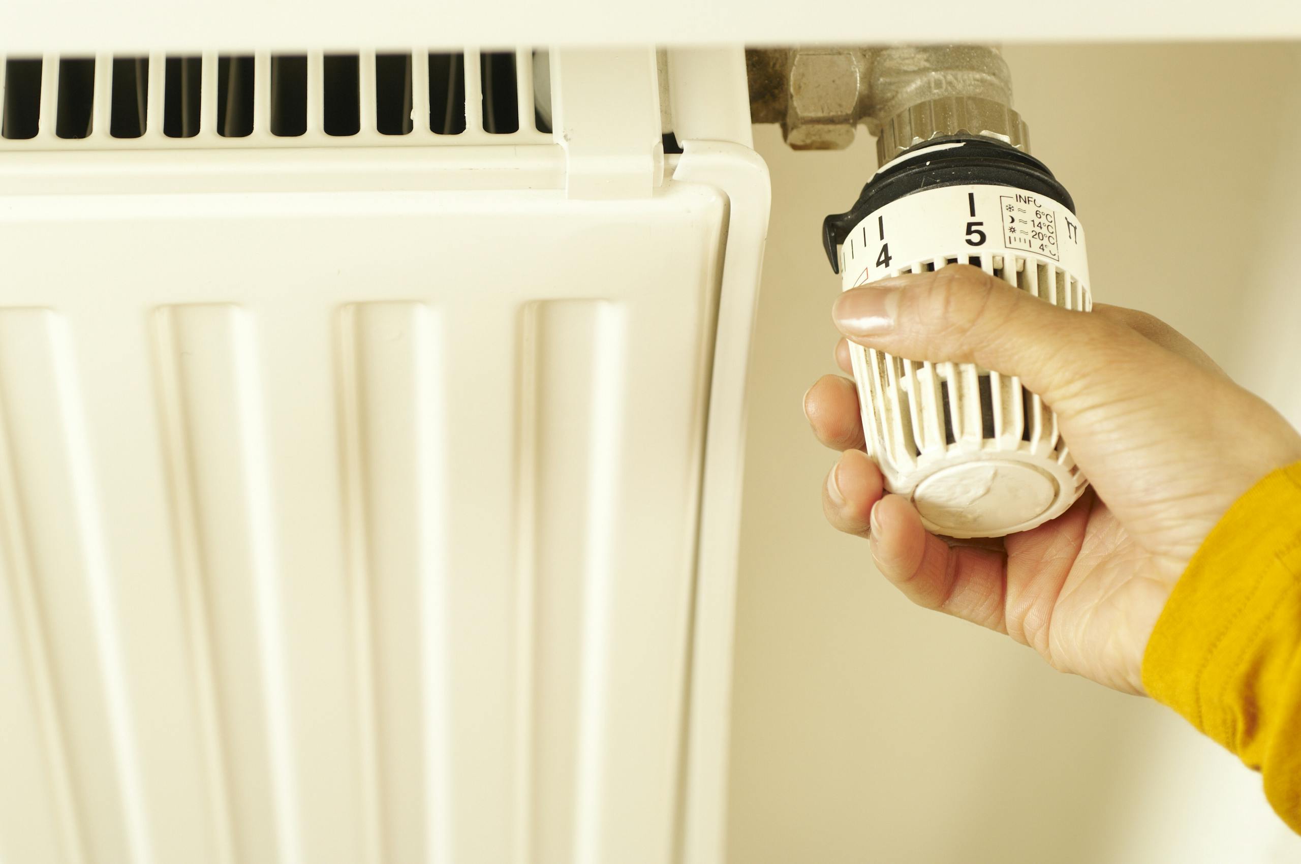 Close-up of hand adjusting radiator thermostat to control home heating temperature.